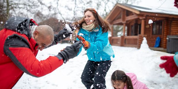Family having fun playing in the snow near a wooden cabin.