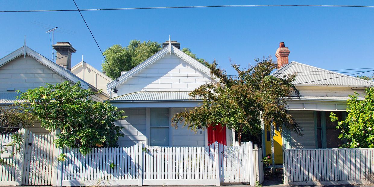 Row of quaint houses with white picket fences and colorful doors under a clear blue sky.