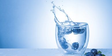 Blueberries splashing into a glass of water with droplets around.