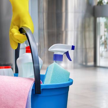 Hand holding cleaning supplies bucket with gloves.