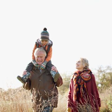 Grandparents enjoying a sunny day outdoors with their grandchild on grandpa's shoulders.