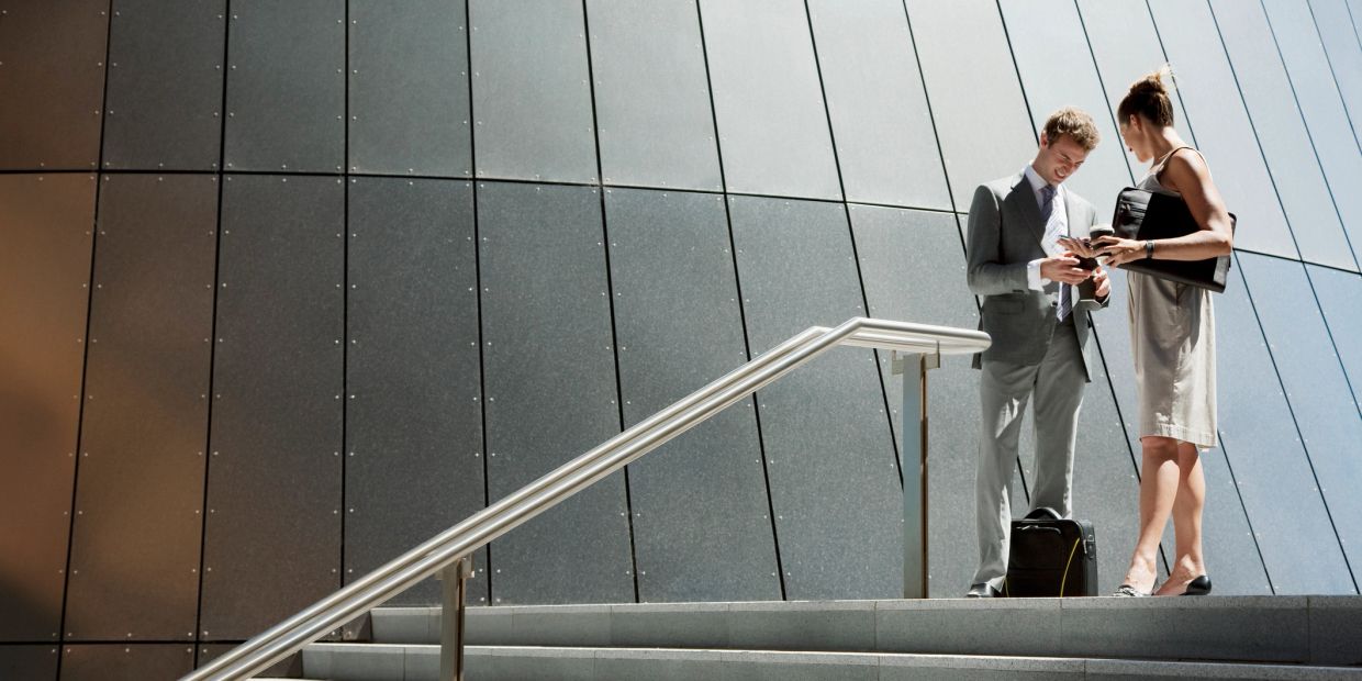 Two businesspeople reviewing documents on stairs outside an office building.