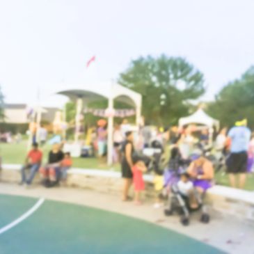 A blurry outdoor gathering with people socializing near tents and trees.