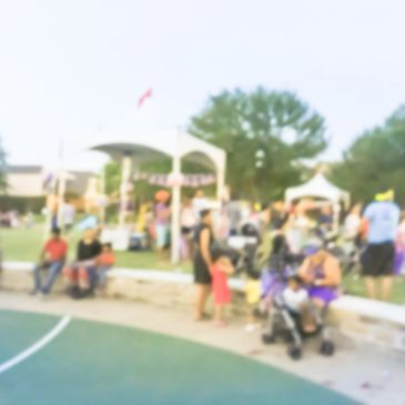 A blurry outdoor gathering with people socializing near tents and trees.