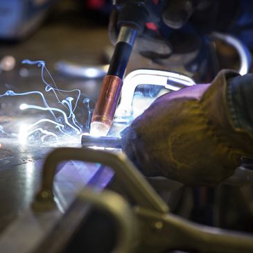 Close-up of welding sparks and gloved hands working on metal.