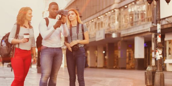 Three young people filming and exploring a city street together.
