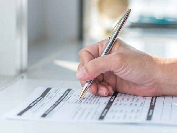 Person filling out a form with a pen on a desk.