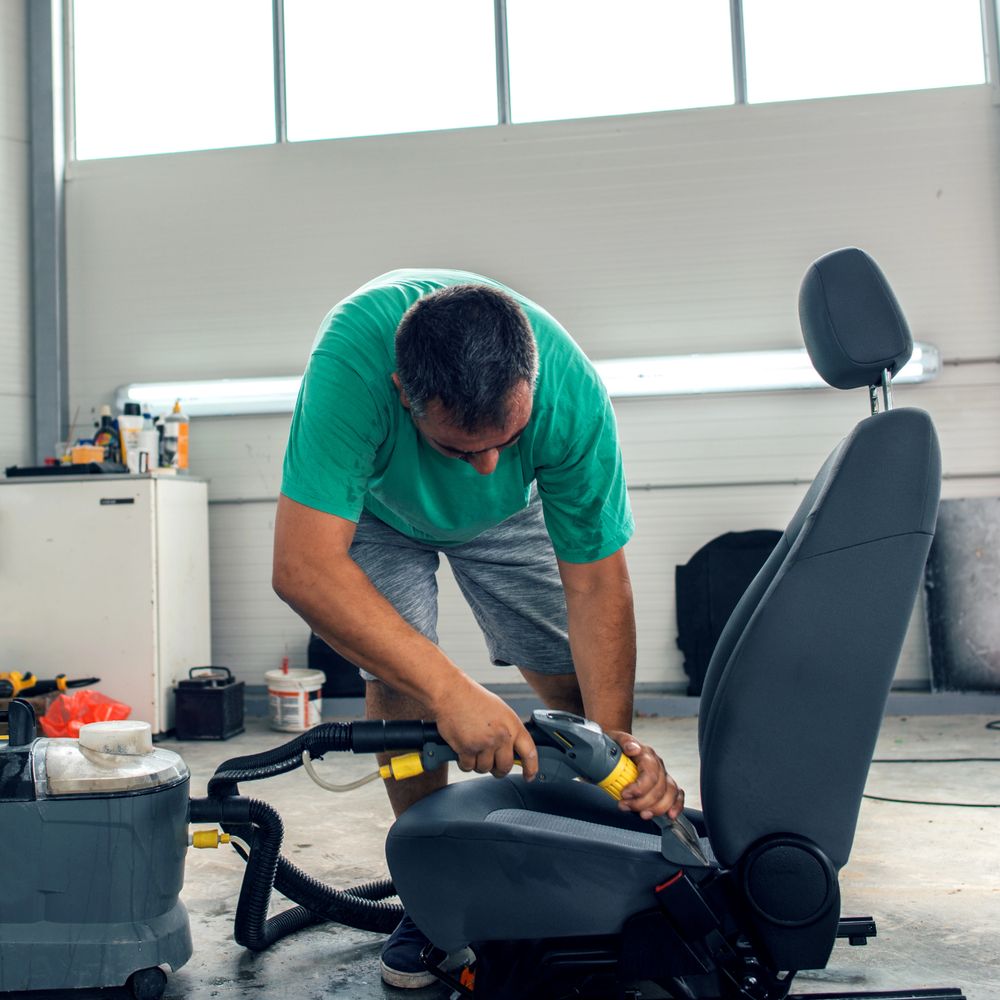 Man cleaning a car seat with a steam cleaner in a garage.