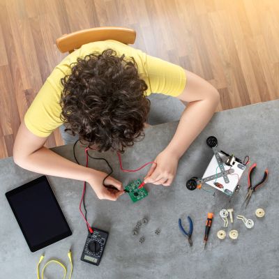 Child assembling an electronic circuit board with tools and components on a table.