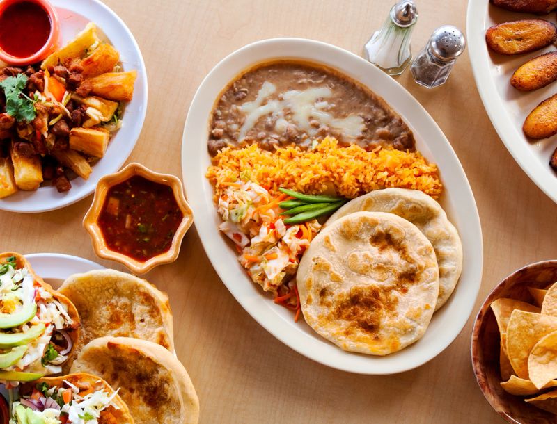 Overhead shot of an El Salvadoran dinner with pupusas, fried plantains, tortilla chips, and yucca.