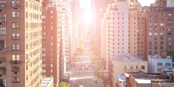 Sunlight brightens a busy city street lined with tall buildings.