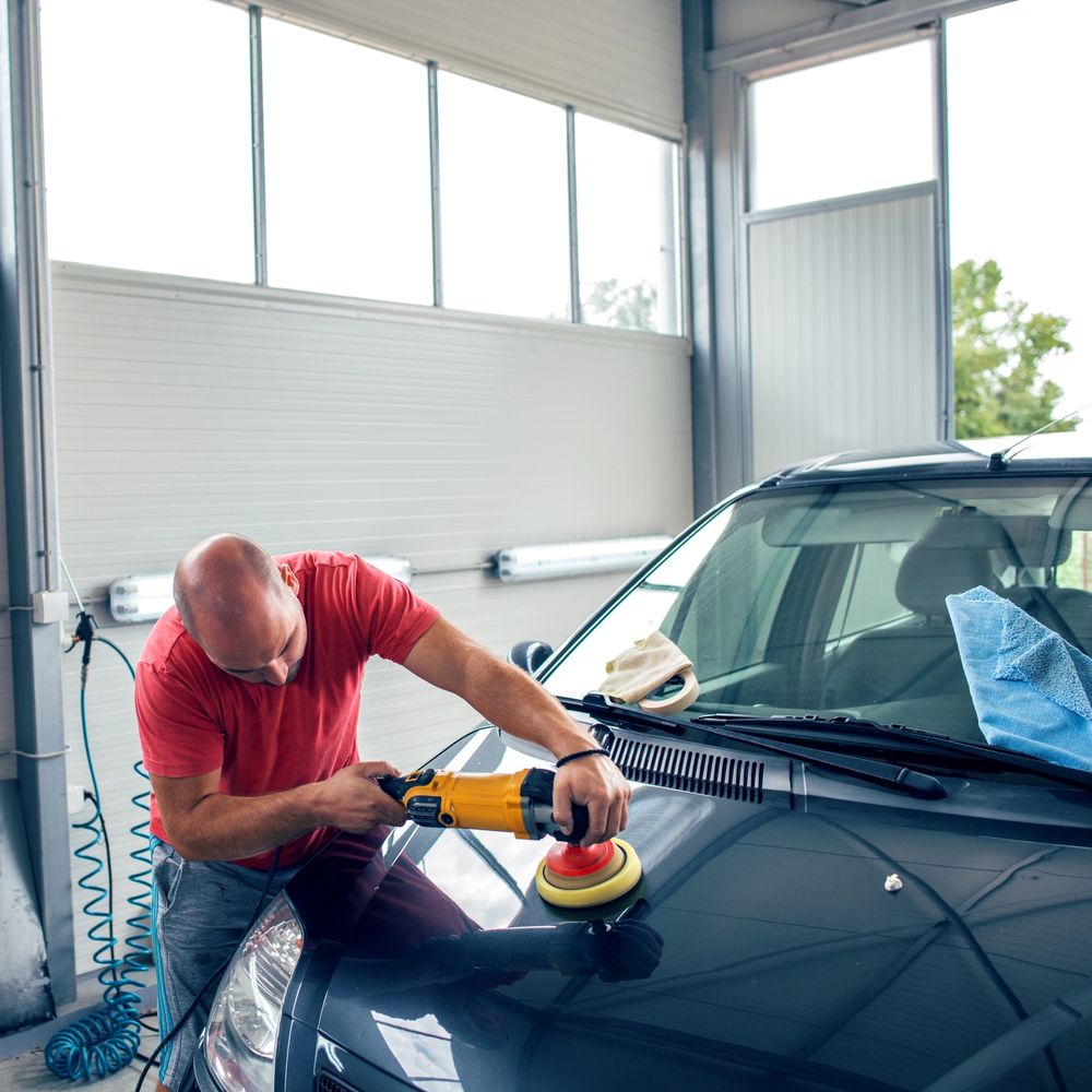 Man polishing a black car hood with an electric buffer.