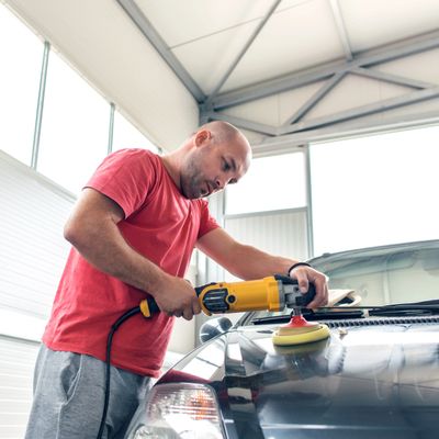 Man polishing a car hood with an electric buffer in a garage.