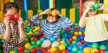 Three children playing joyfully in a colorful ball pit.