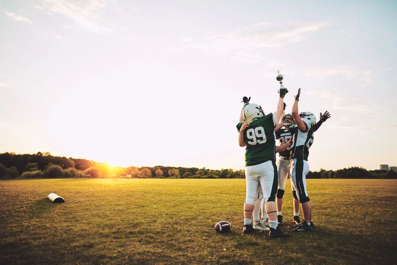 Ecstatic group of American football players standing in a huddle and raising a championship trophy in celebration