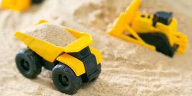 Yellow toy dump truck and bulldozer playing in sand.