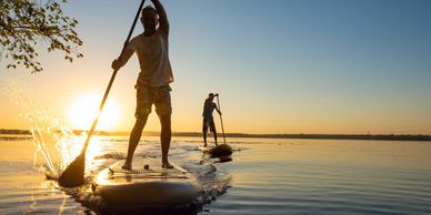 Two people paddleboarding on calm water at sunset.