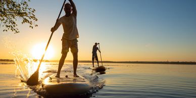 Two people paddleboarding on calm water during sunset.