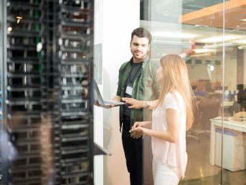 Two coworkers discussing work near a server rack in an office.