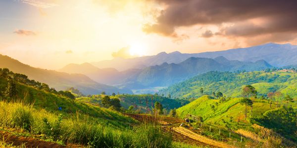 Sunset over lush green hills and distant mountains.