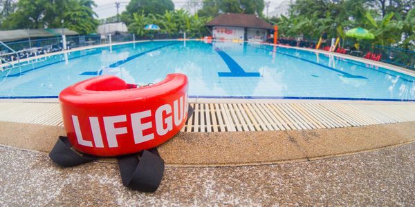 Red lifeguard float rests beside a calm swimming pool on a cloudy day.
