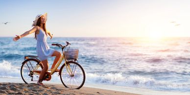 Woman in white dress enjoying a bike ride by the beach at sunset.