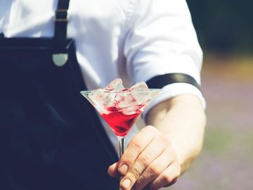 Bartender holding a cocktail glass filled with red drink and ice.