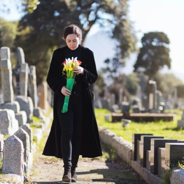 Woman holding flowers, walking in a cemetery.
