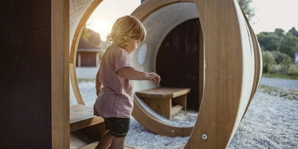 A young child playing inside a wooden circular structure outdoors.