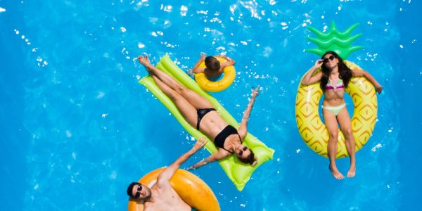 People relaxing on colorful pool floats in a bright blue pool.