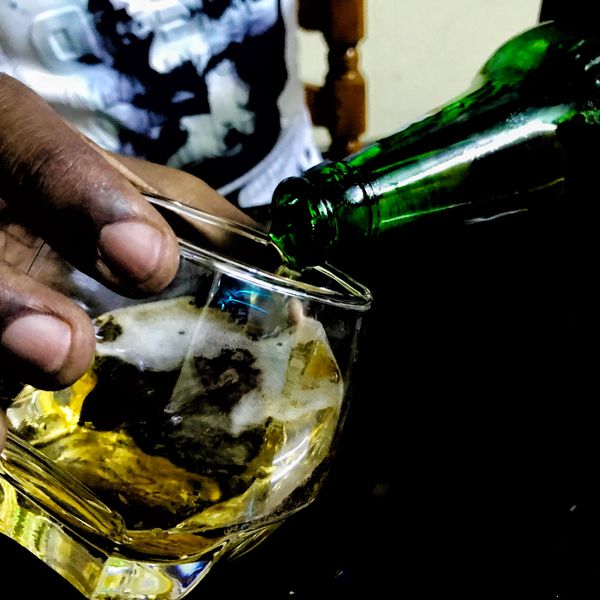 a black hand holding a glass pouring a beer into it