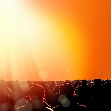 Crowd of people silhouetted against a bright, warm orange sunset.