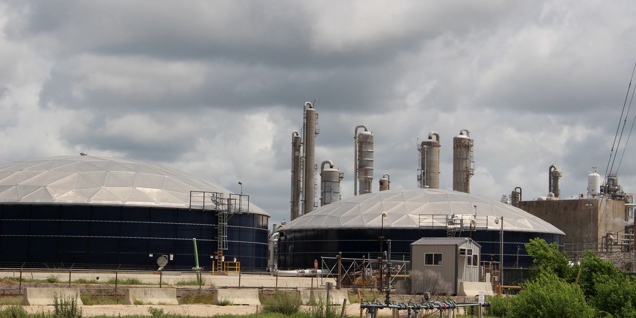 Industrial storage tanks and refinery towers under a cloudy sky.