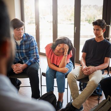 Teenagers in a serious group discussion, some showing signs of stress or discomfort.