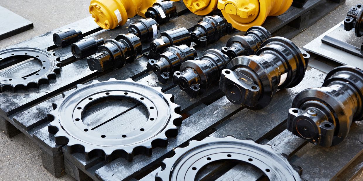Heavy machinery parts arranged on pallets, including sprockets and rollers.