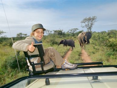 Boy giving thumbs up on a safari with elephants in the background.