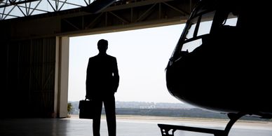 Silhouette of a businessman with briefcase near helicopter in hangar.