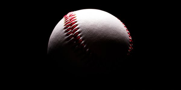 A baseball partially illuminated against a dark background.