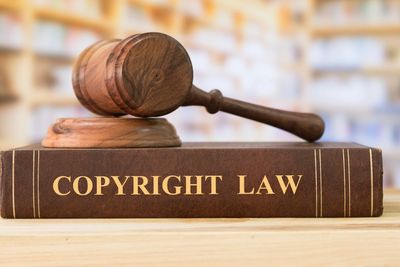 Wooden gavel resting on a thick book titled 'Copyright Law'.