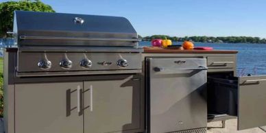 Modern outdoor kitchen setup with grill and fridge by the water.
