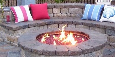 Stone fire pit with seating and colorful cushions outdoors.