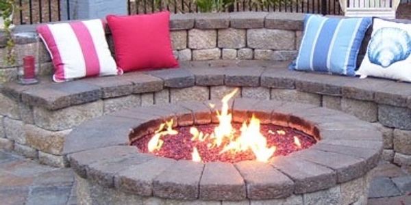 Stone fire pit with seating and colorful cushions outdoors.