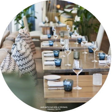 Elegant dining tables set with blue glasses and patterned cushions in a cozy restaurant.