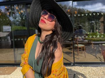 Woman in large black hat and sunglasses outdoors.