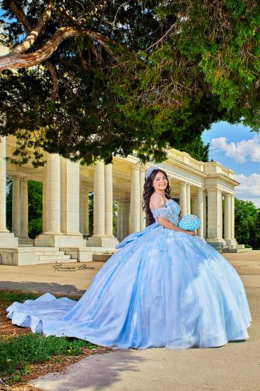 Joven en vestido azul posando junto a una estructura clásica.