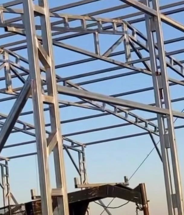 Steel frame structure being assembled outdoors on a clear day.