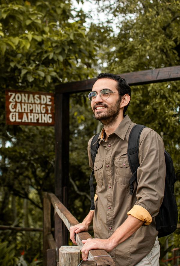 A smiling man with glasses and backpack at a camping and glamping zone.