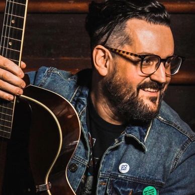 Man with glasses playing acoustic guitar, smiling.