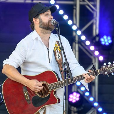 Man in white shirt playing acoustic guitar on stage with microphone.