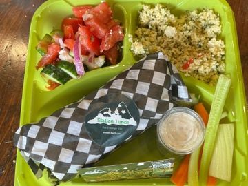 A healthy lunch tray with a wrapped sandwich, salad, couscous, and veggies.